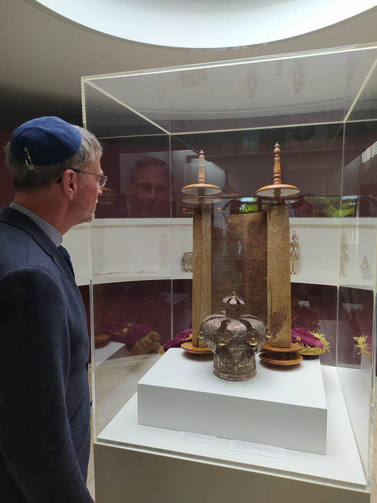 Das Bild zeigt Prof. Ballhorn vor einer Vitrine mit einer Torarolle