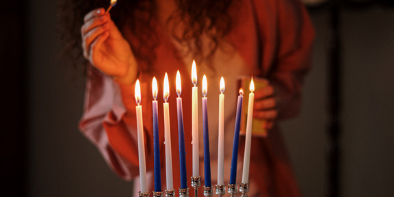 Das Bild zeigt eine Person, die Kerzen in einem Leuchter anzündet. 