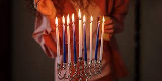 Das Bild zeigt eine Person, die Kerzen in einem Leuchter anzündet. 