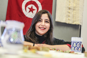 Eine internationale Studierende lächelt in die Kamera. Im Hintergrund hängt eine Tunesienflagge.