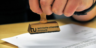 Symbolbild Stempel Nahaufnahme einer Hand, die einen Stempel der TU hält.