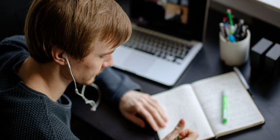 Ein Student arbeitet mit Laptop und Notizbuch.