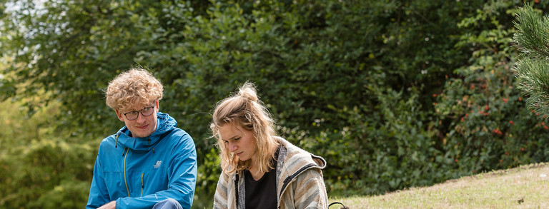 Studierende auf dem grünen Campus Zwei Studierende sitzen im Grünen.
