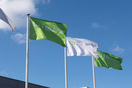 Grüne und weiße Flaggen mit der Inschrift „TU 50 Jahre“ vor blauem Himmel